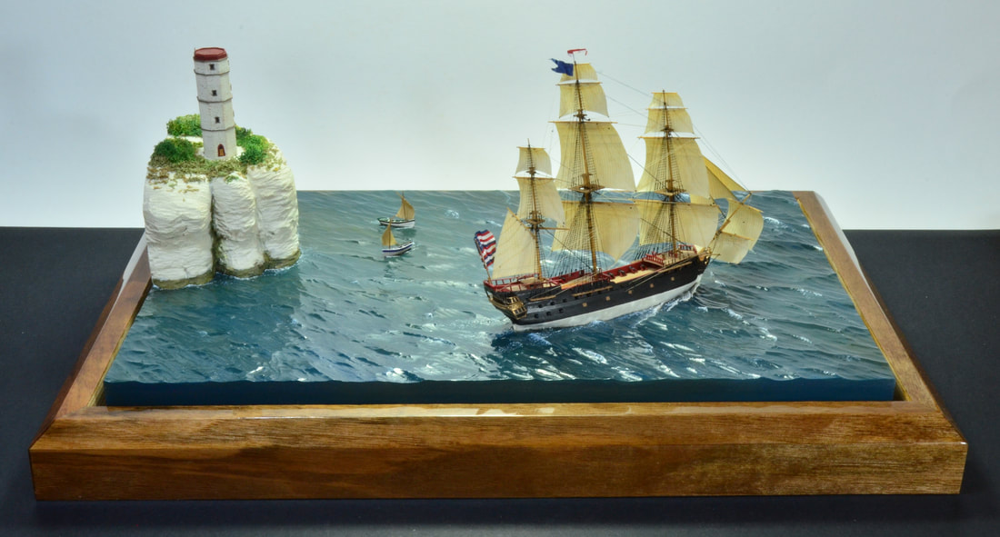 Miniature model diorama of the Bonhomme Richard passing Flamborough LIghthouse while two fishing cobles sail nearshore.
